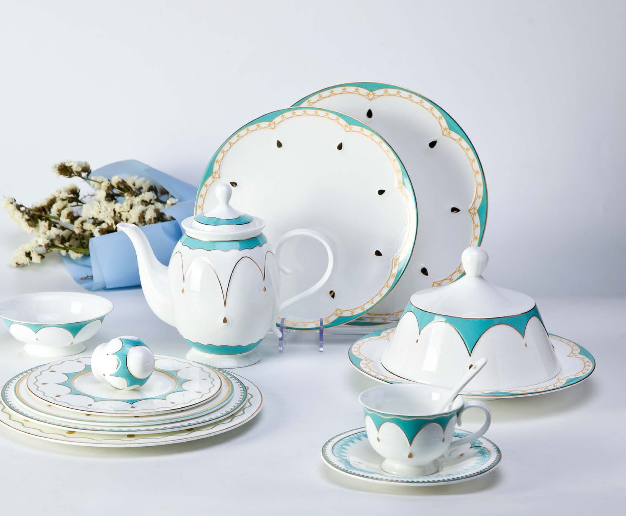 A comprehensive luxury porcelain dinnerware set featuring turquoise scalloped edges and gold detailing on a white bone china base.