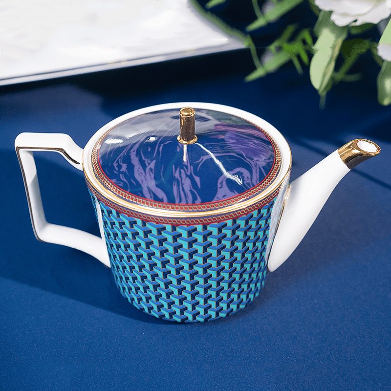 A premium porcelain teapot featuring a blue 3D geometric pattern and gold trim on a dark blue table setting.