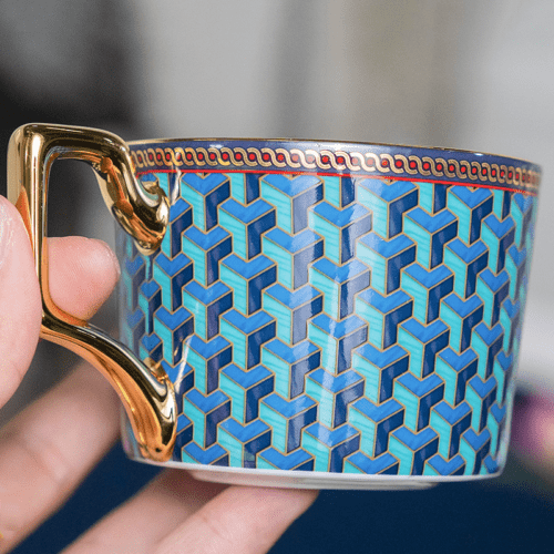 A luxury porcelain teacup featuring a vibrant blue 3D geometric pattern and an ornate gold handle.