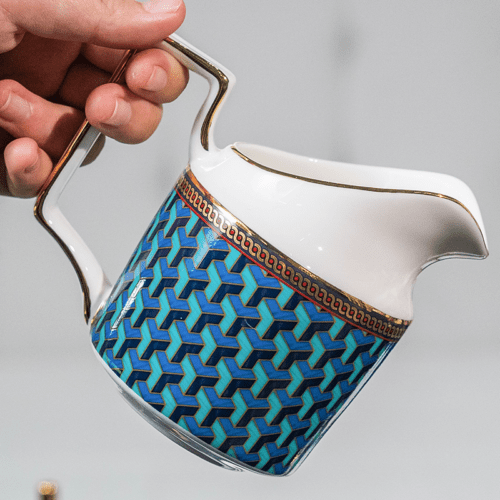 A luxury porcelain milk pitcher featuring a blue 3D geometric pattern and a gold-rimmed spout and handle.