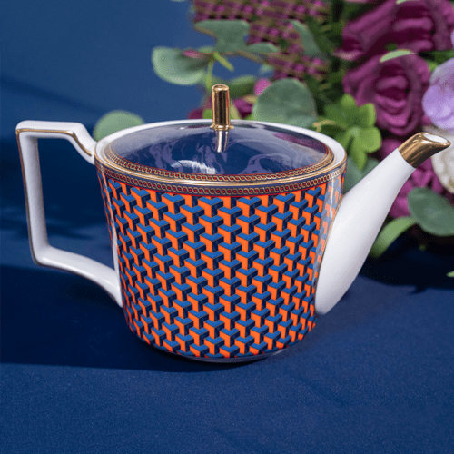 A luxury porcelain teapot featuring a vibrant orange and blue 3D geometric pattern with gold trim on a dark blue background.