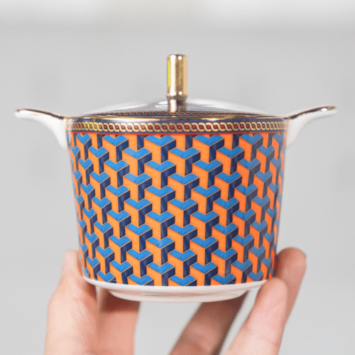 A luxury porcelain sugar bowl featuring a vibrant orange and blue 3D geometric pattern and a gold lid finial.