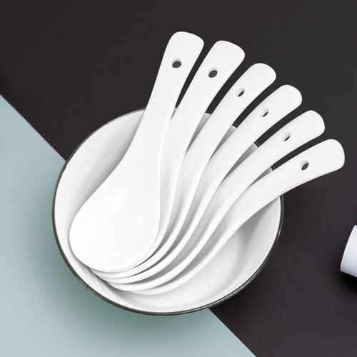 Galaxy pure white commercial ceramic soup spoons set neatly stacked inside a white porcelain bowl on a split black and grey surface.