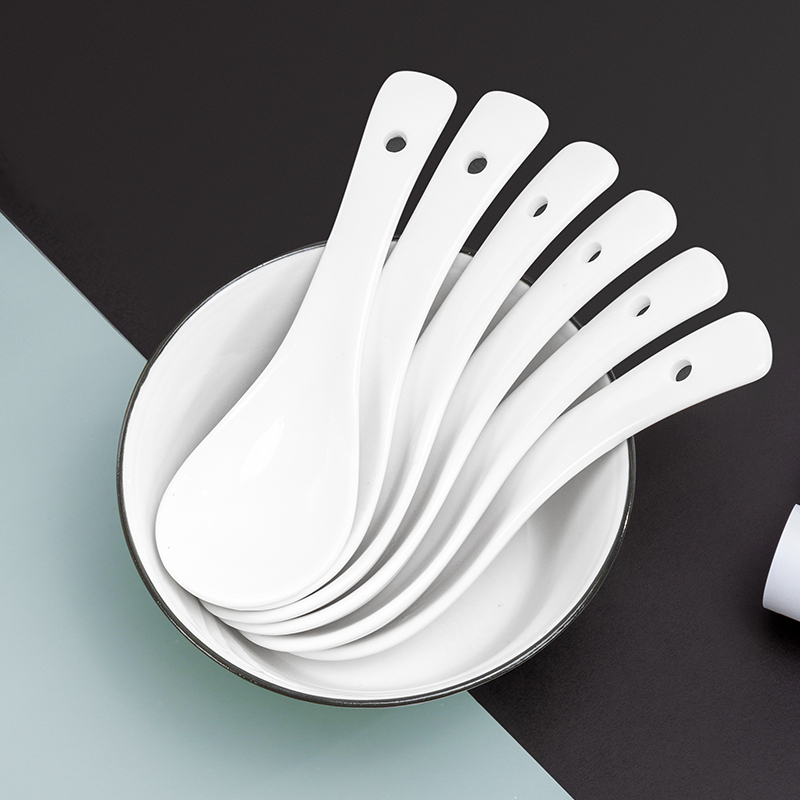Galaxy pure white commercial ceramic soup spoons set neatly stacked inside a white porcelain bowl on a split black and grey surface.