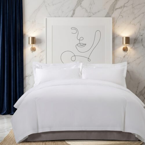 Luxury white hotel duvet cover and pillow sham set styled on a king bed against a marble wall with gold sconce lighting and navy blue curtains in a modern boutique bedroom