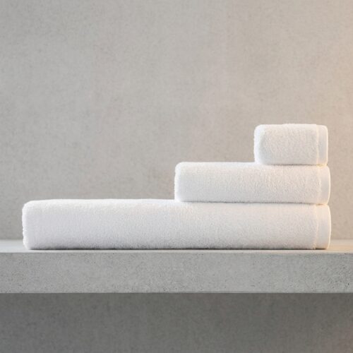 Set of three neatly folded luxury white hotel towels including a bath towel, hand towel, and face towel displayed on a gray concrete surface