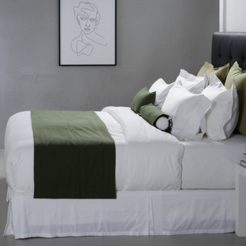 A luxury white hotel bed layered with a solid olive green bed runner and matching green accent pillows against a dark headboard.