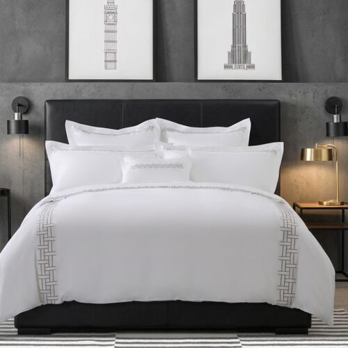Luxury white hotel duvet cover set with gray Greek key lattice embroidery border styled on a king bed with black leather headboard in a modern bedroom