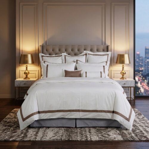 A luxury hotel bed featuring white linens with bronze-brown borders, gold bedside lamps, and a tufted headboard.
