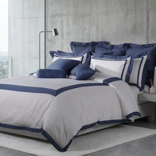 Luxury grey and navy border hotel duvet cover set styled on a king bed with matching navy pillow shams and decorative cushions in a modern concrete-wall bedroom