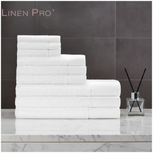 12-piece luxury white hotel towel set including bath towels, hand towels, face towels and guest towels neatly stacked in a stepped arrangement on a white marble surface with a reed diffuser beside them