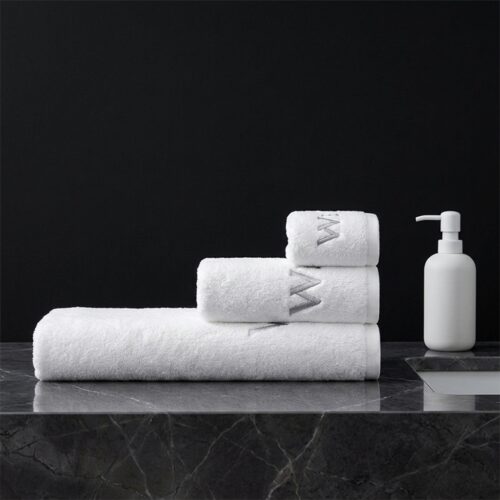 A neat stack of white hotel towels featuring grey monogrammed letter embroidery on a black marble countertop next to a white soap dispenser.