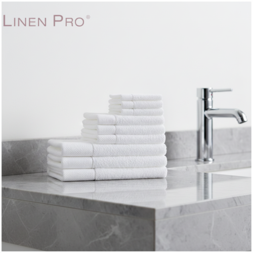 A neat pyramidal stack of plush white hotel towels with textured dobby borders on a polished grey marble vanity.