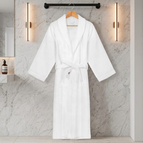 A luxury white plush hotel bathrobe hanging on a wooden hanger against a modern white marble wall with vertical sconces.