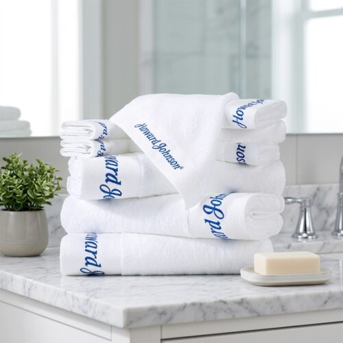 A stack of white cotton hotel towels featuring custom "Howard Johnson" blue script embroidery on a marble bathroom vanity.