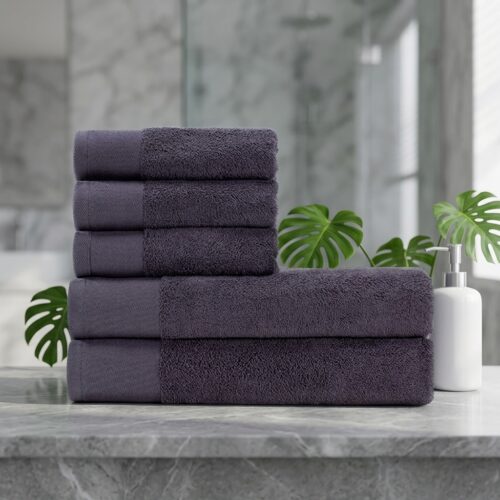 A neatly stacked set of luxury deep purple cotton hotel towels on a grey marble vanity countertop next to a white soap dispenser.
