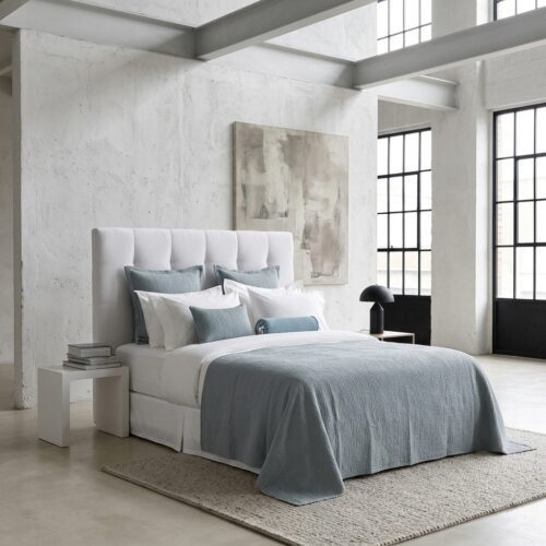 A luxury hotel bed featuring a sage green textured coverlet, matching Euro shams, and crisp white linens in a modern industrial-style room.