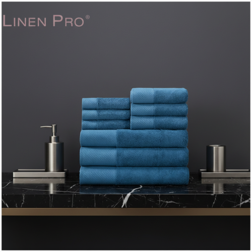 A stack of plush deep blue hotel towels featuring a textured dobby border on a black marble countertop.