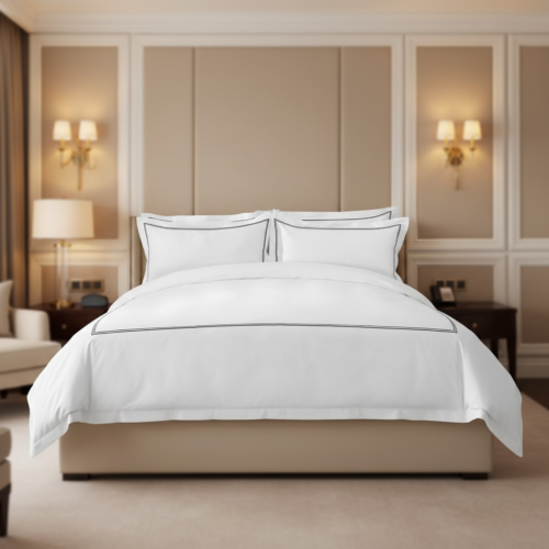 A luxury white hotel bed featuring thin dark grey triple bourdon stitch embroidery on the duvet and pillows against a beige upholstered wall.