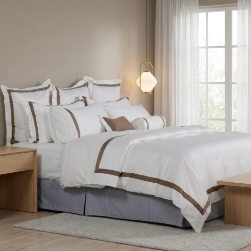 A luxury hotel bed featuring white linens with bronze-brown border embroidery and modern bedside pendant lighting.