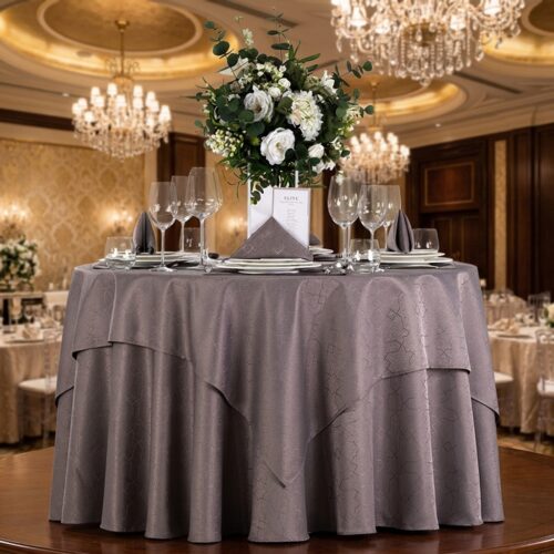 Elegant round mauve gray jacquard tablecloth styled with crystal wine glasses, folded linen napkins, and a white rose floral centerpiece in a luxury hotel ballroom