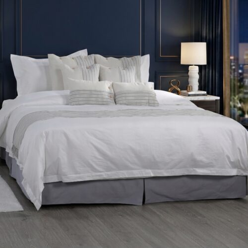 A luxury boutique hotel king bed dressed in crisp white comforter with blue and white ticking stripe accent pillows and a matching fringed bed runner against a navy blue paneled wall.
