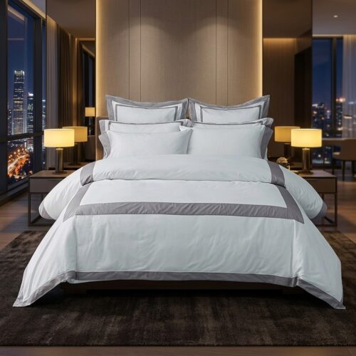 A luxury high-rise hotel king bed dressed in crisp white linens with a wide slate-grey stitched border frame duvet cover against a night city skyline view.