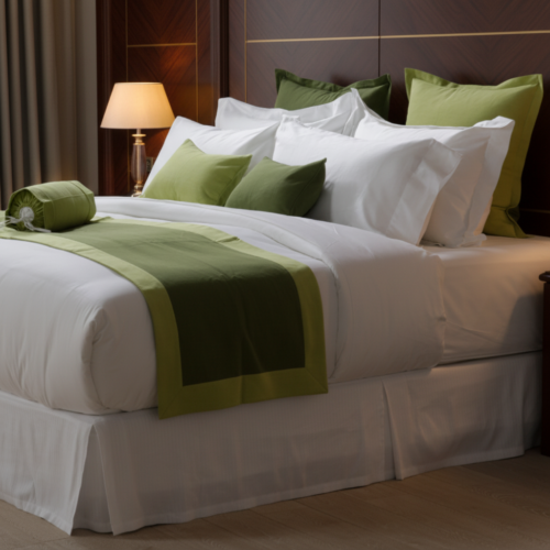 A luxury hotel king bed dressed in crisp white linens, featuring an olive green bed runner with lime green trim and matching green accent pillows.