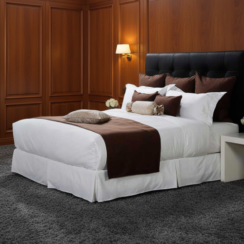 A luxury hotel king bed dressed in crisp white linens, featuring a solid color bed runner and matching chocolate brown accent cushions against a tufted black headboard.