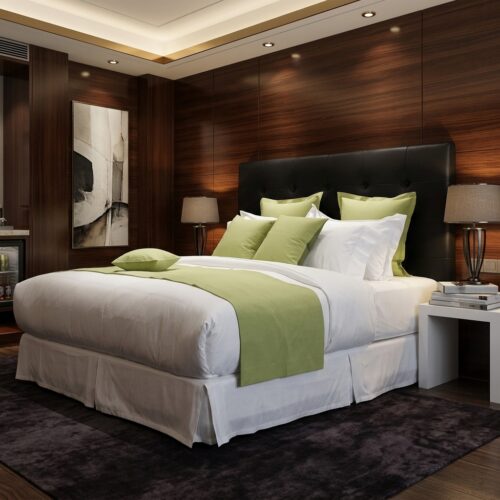 A luxury hotel king bed dressed in crisp white linens, featuring a lime green bed runner and coordinating green accent pillows against a tufted black headboard.