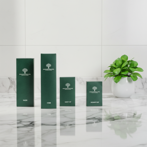 Four forest green eco-friendly hotel amenity boxes standing upright in a line on a polished white marble countertop.