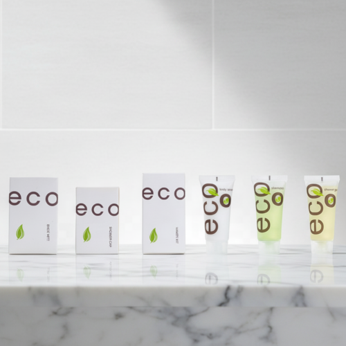 A line of eco-friendly white hotel amenity boxes and small green liquid tubes on a reflective marble counter.