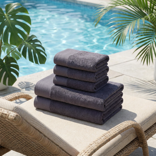 A neat stack of plush charcoal grey luxury hotel towels arranged on a woven wicker poolside lounge chair next to turquoise pool water.