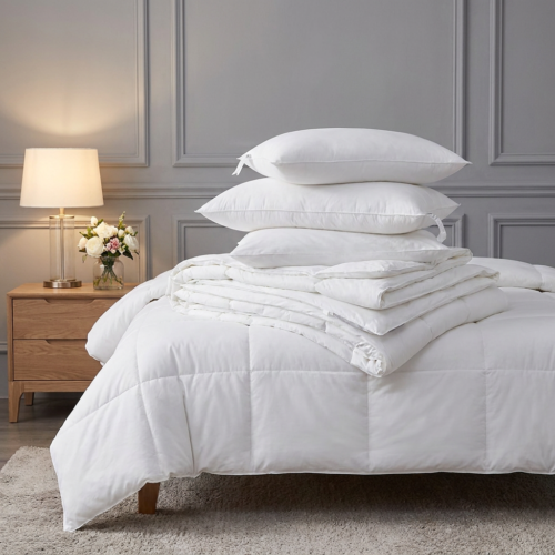A stacked arrangement of three plush white microfiber hotel pillows resting on a neatly folded box-stitch duvet insert over a dressed guest bed.