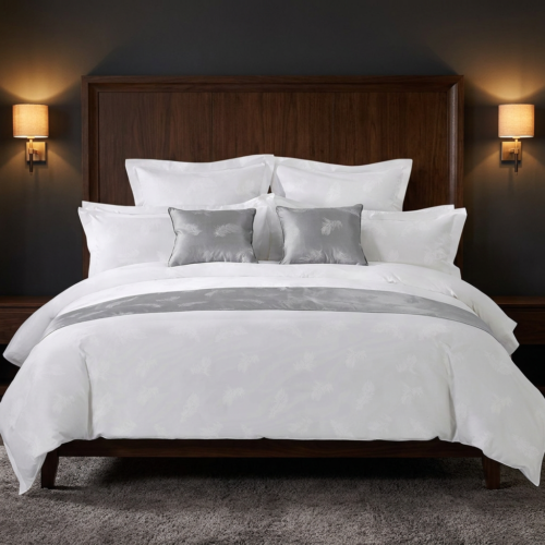 A luxury hospitality king bed dressed in white feather jacquard linens with a silver grey bed runner and matching accent cushions against a dark wood headboard.