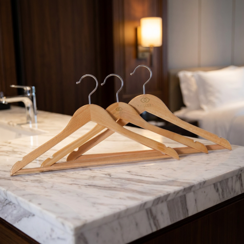 A trio of luxury natural wood hotel coat hangers with silver metal hooks displayed on a white marble countertop in a guest room.