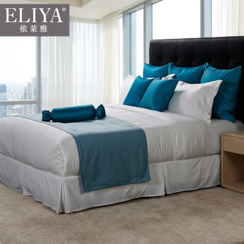 ELIYA premium white hotel bed bedding set with a teal blue bed runner and matching decorative cushions against a tufted black leather headboard.