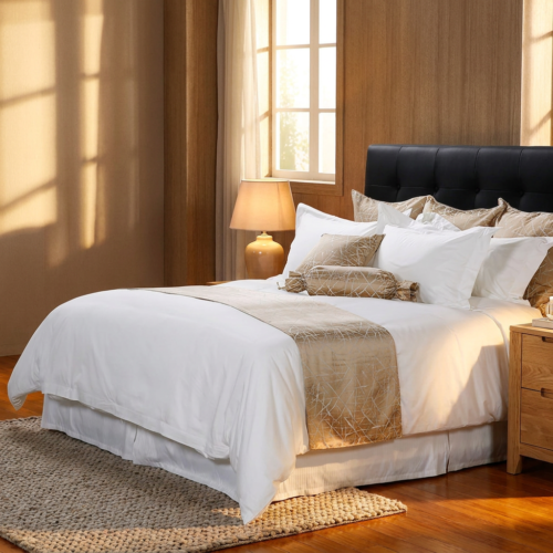 A luxury hotel bed styled with crisp white sateen linens, a champagne gold geometric bed runner, and matching decorative accent pillows.