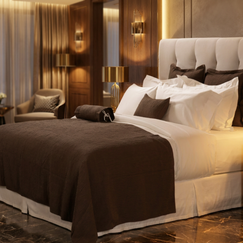 Galaxy premium white hotel bedding layered with a deep chocolate brown textured coverlet and accent pillows against a tufted headboard.