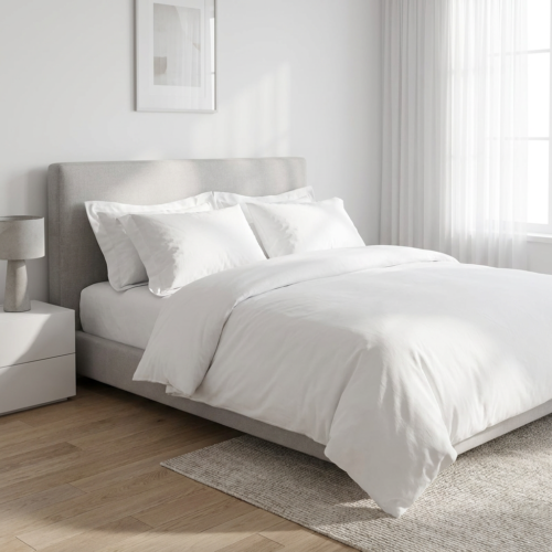 Galaxy premium minimalist pure white hotel duvet cover set with layered white pillowcases on a grey upholstered bed in a sunlit modern guest suite.