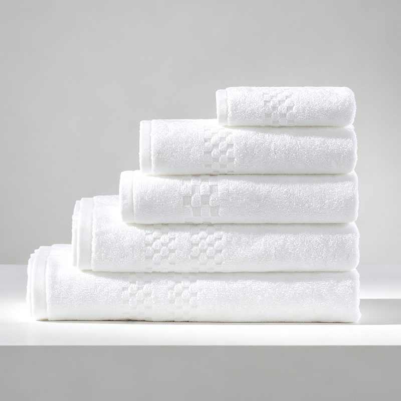 Stack of five folded white 100% cotton hotel towels with a textured checkerboard jacquard border.