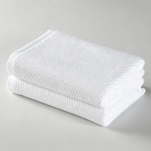 Stack of two folded white 100% cotton hotel bath towels featuring a textured honeycomb waffle weave pattern.