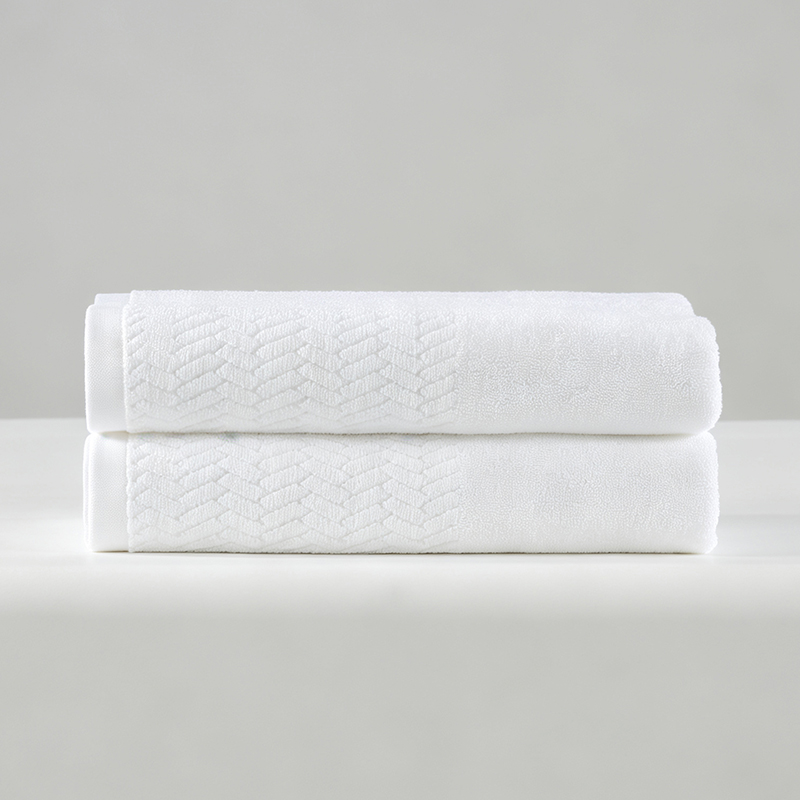 Folded stack of two white 100% cotton hotel towels featuring a textured herringbone jacquard woven border.