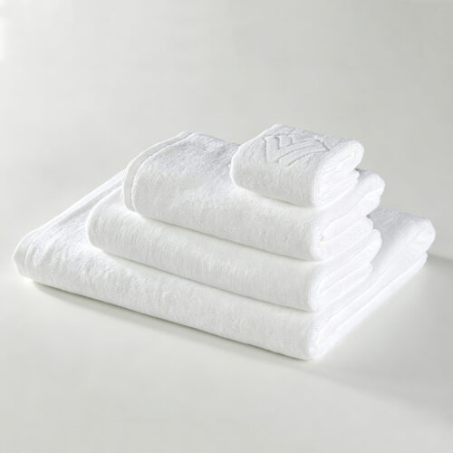 Stack of folded white 100% cotton hotel towels featuring an embossed woven logo on top.