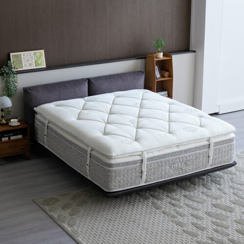 White quilted hotel mattress topper pad with elastic anchor straps installed on a hotel bed.