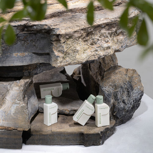Galaxy luxury botanical hotel toiletry bottles set including body wash, shampoo, conditioner, and lotion nestled among natural grey rock stones.