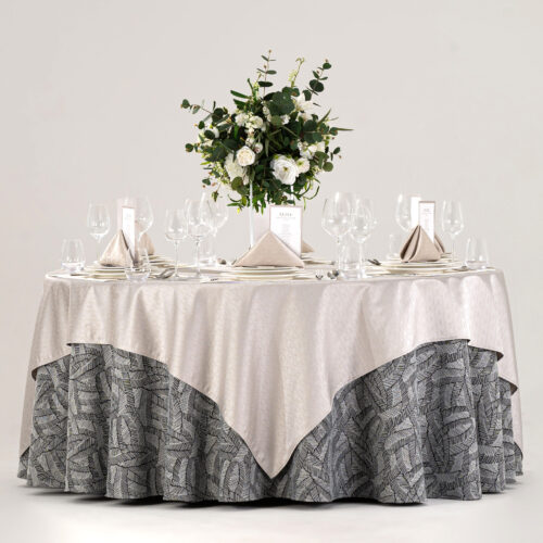 Hotel round banquet table styled with an ivory square overlay, black and white feather jacquard skirt, placemats, and green floral centerpiece.