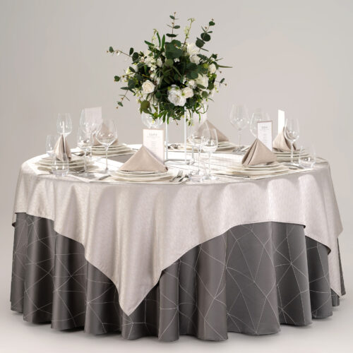 Hotel round banquet table styled with a dark grey geometric skirt, silver overlay, stitched placemats, folded napkins, and green floral centerpiece.