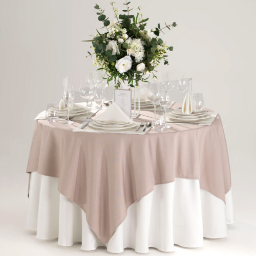 Hotel round banquet table styled with a white base skirt, textured blush pink square overlay, white placemats, folded napkins, and green floral centerpiece.