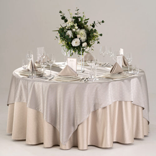 Gallery showcase of a round hotel banquet table styled with champagne skirt, silver overlay, embroidered placemats, folded napkins, and flatware.